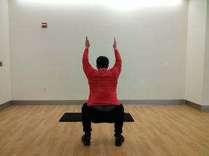 rear view of man in squat position with arms raised straight above head